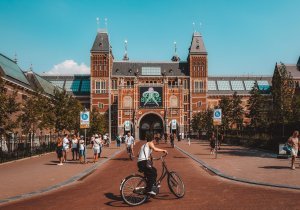 Exterior of the Rijksmuseum in Amsterdam with cyclists and pedestrians in the plaza on a sunny day.