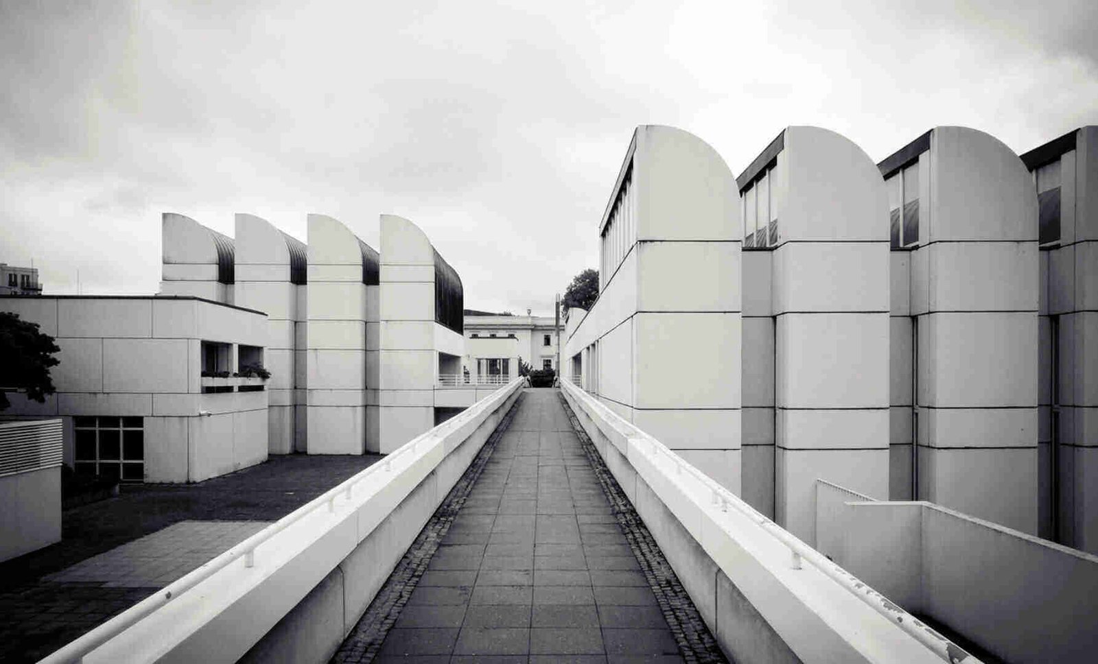 A pathway leading between modern white buildings in black and white.