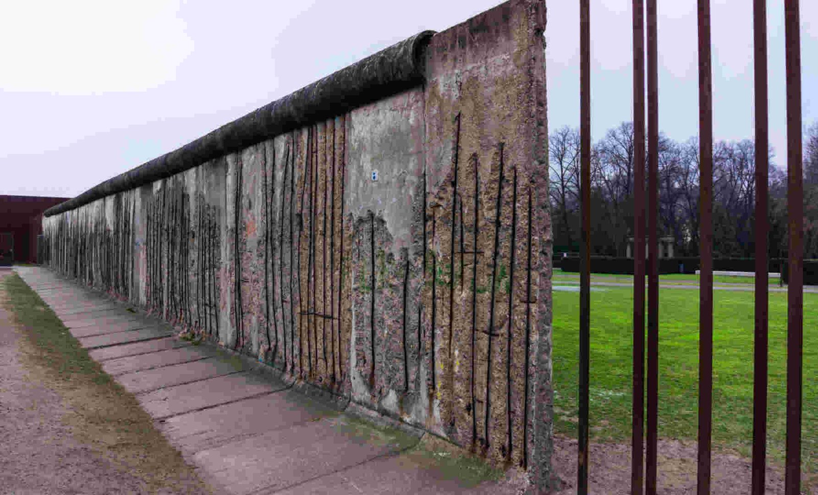 Historical view of the Berlin Wall with grass and trees in the background.