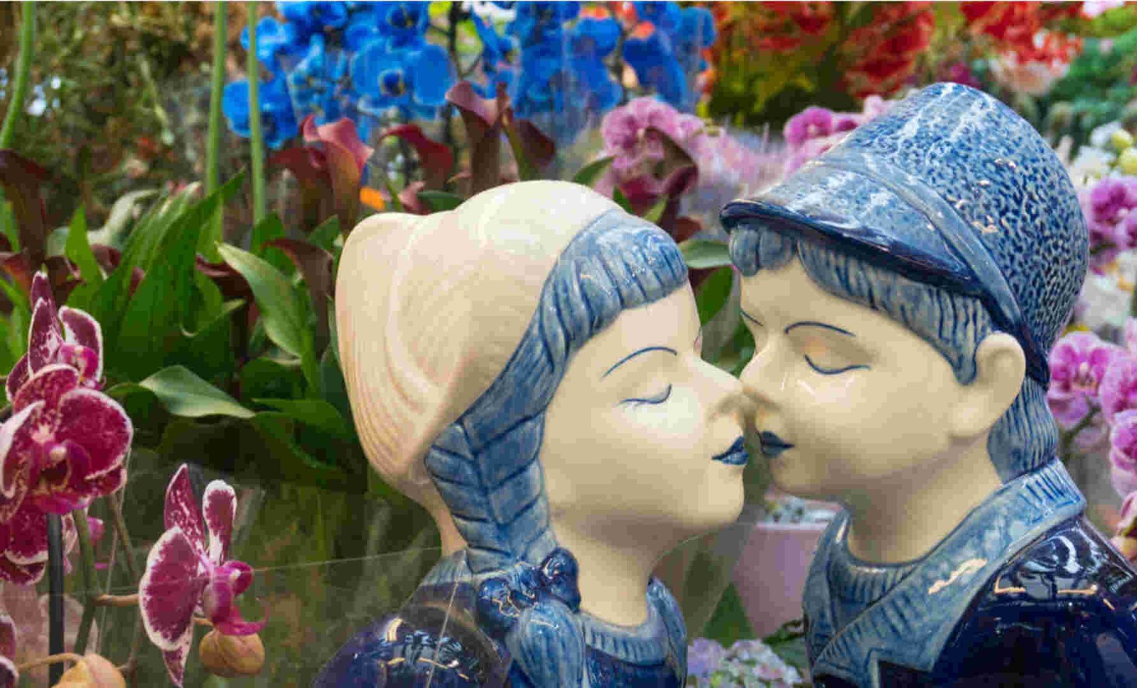 A pair of porcelain figurines of a boy and girl kissing surrounded by colorful flowers.