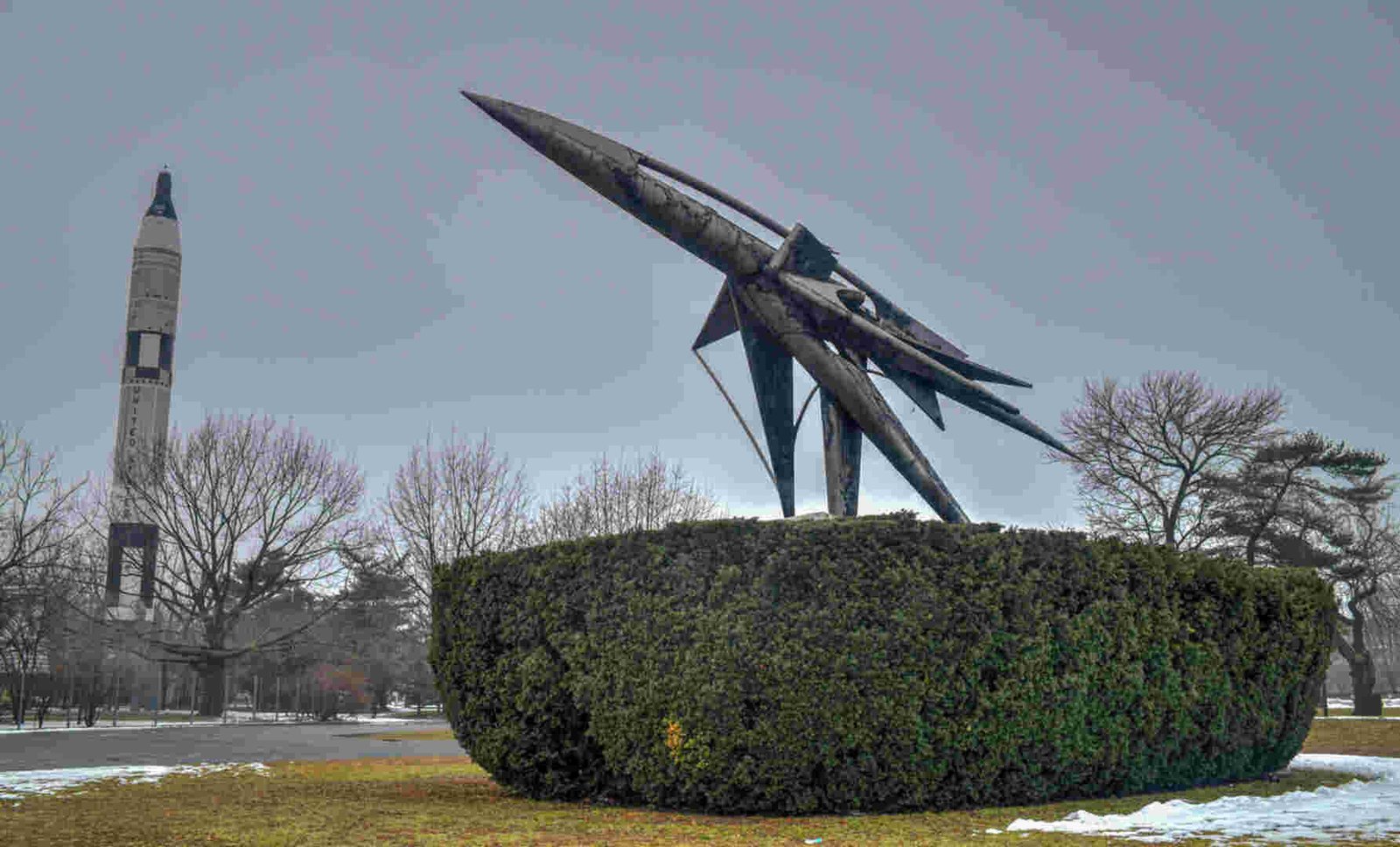 A striking rocket sculpture surrounded by greenery in a park.