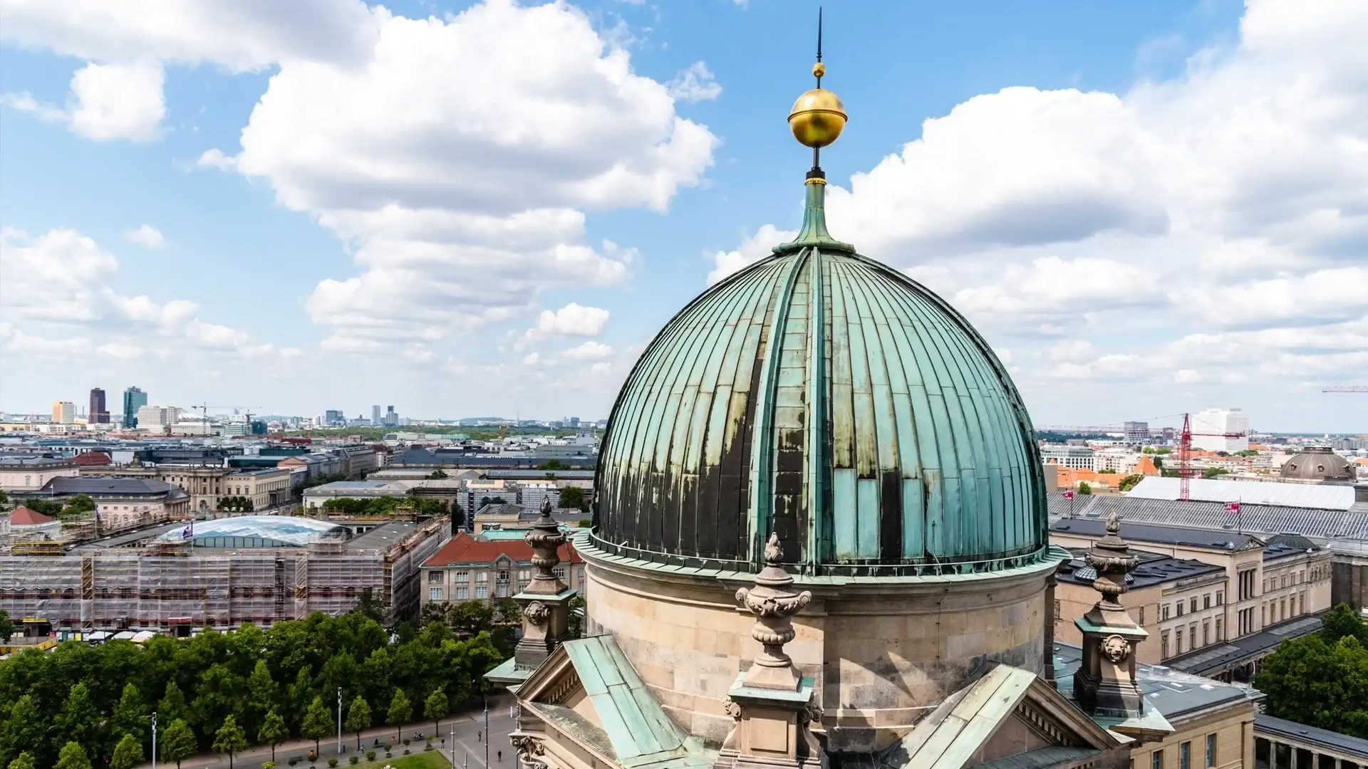 Aerial view of a historic dome in Berlin with a green patina and golden ornament.