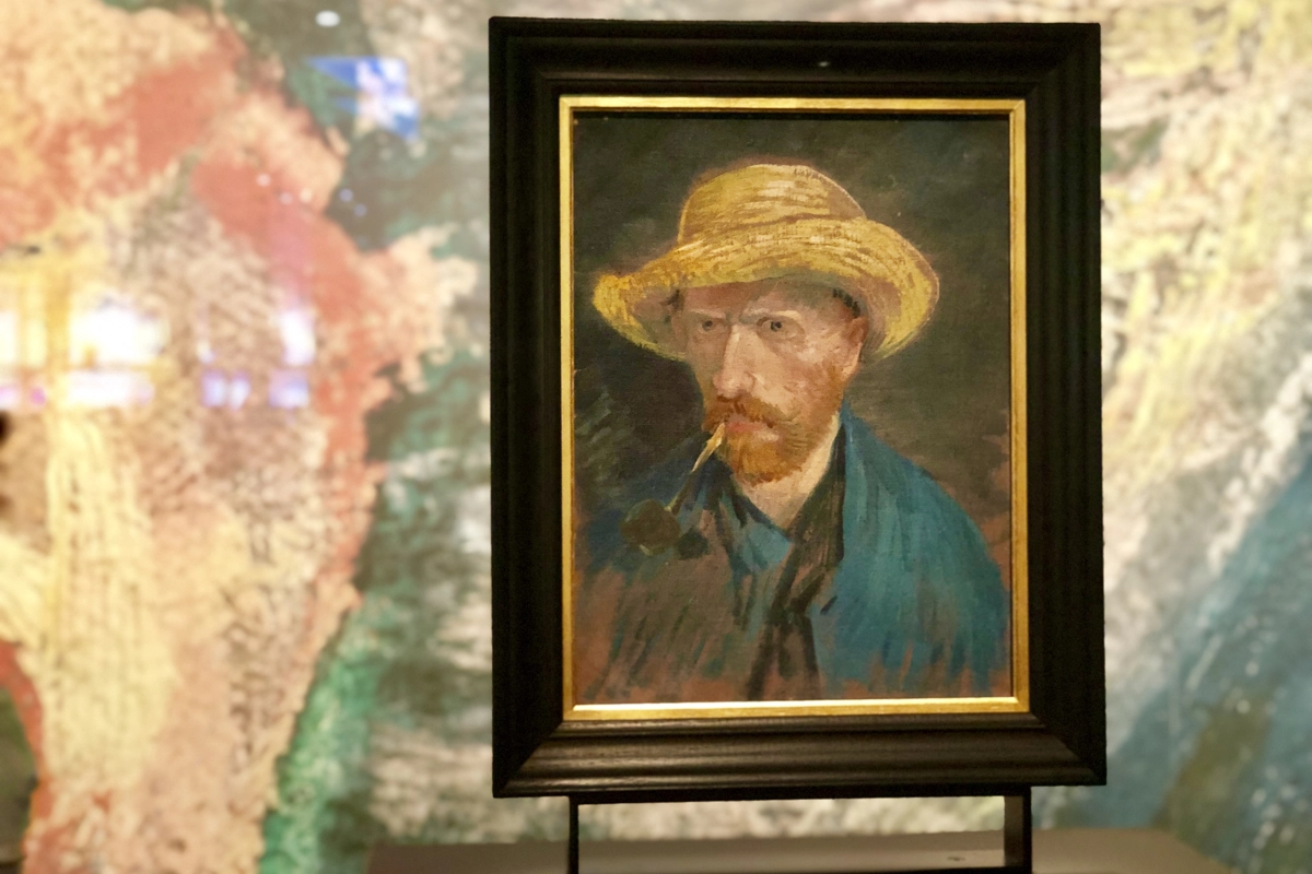 Van Gogh self-portrait in a black frame: the artist in a yellow straw hat with a pipe, set against an artistic backdrop.