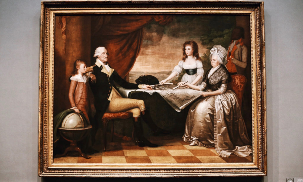 A historic painting depicts a seated woman pointing at a map with a feather pen, accompanied by a standing man in a military uniform, a child, another woman, and a figure in the background. The scene conveys a sense of planning or strategy.