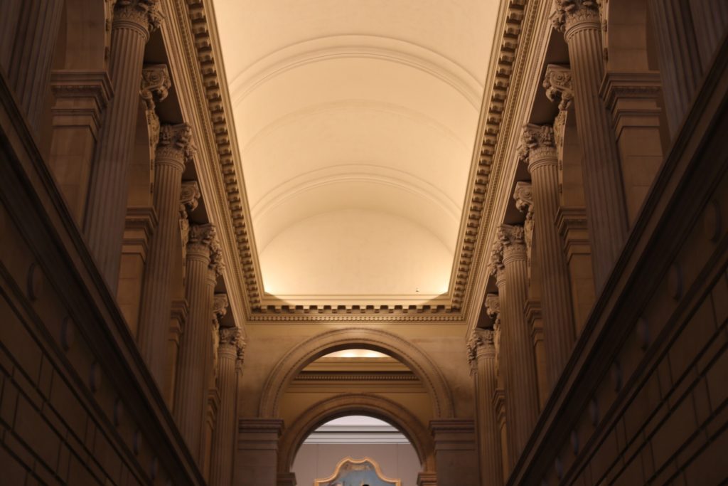Interior view of an elegant, historic building with a curved, vaulted ceiling. The architecture features intricate columns and decorative details, bathed in warm, soft lighting.