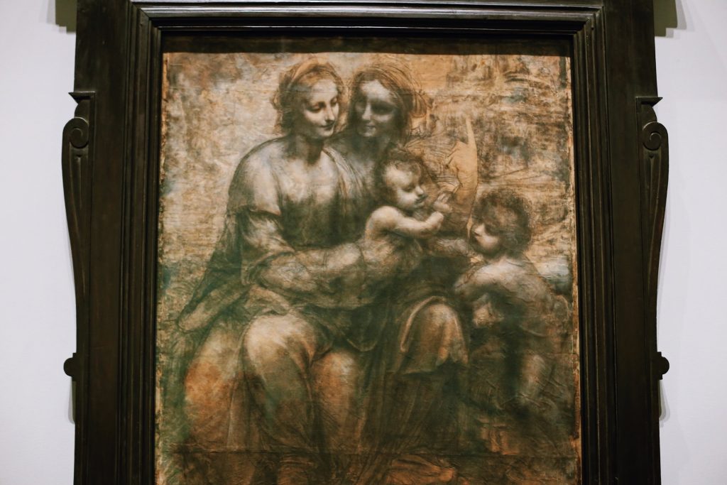 A framed artwork depicts three seated adults and two children in a classical style. The adults and children are arranged closely, evoking a sense of familial interaction. The image has an aged, sepia-toned appearance.