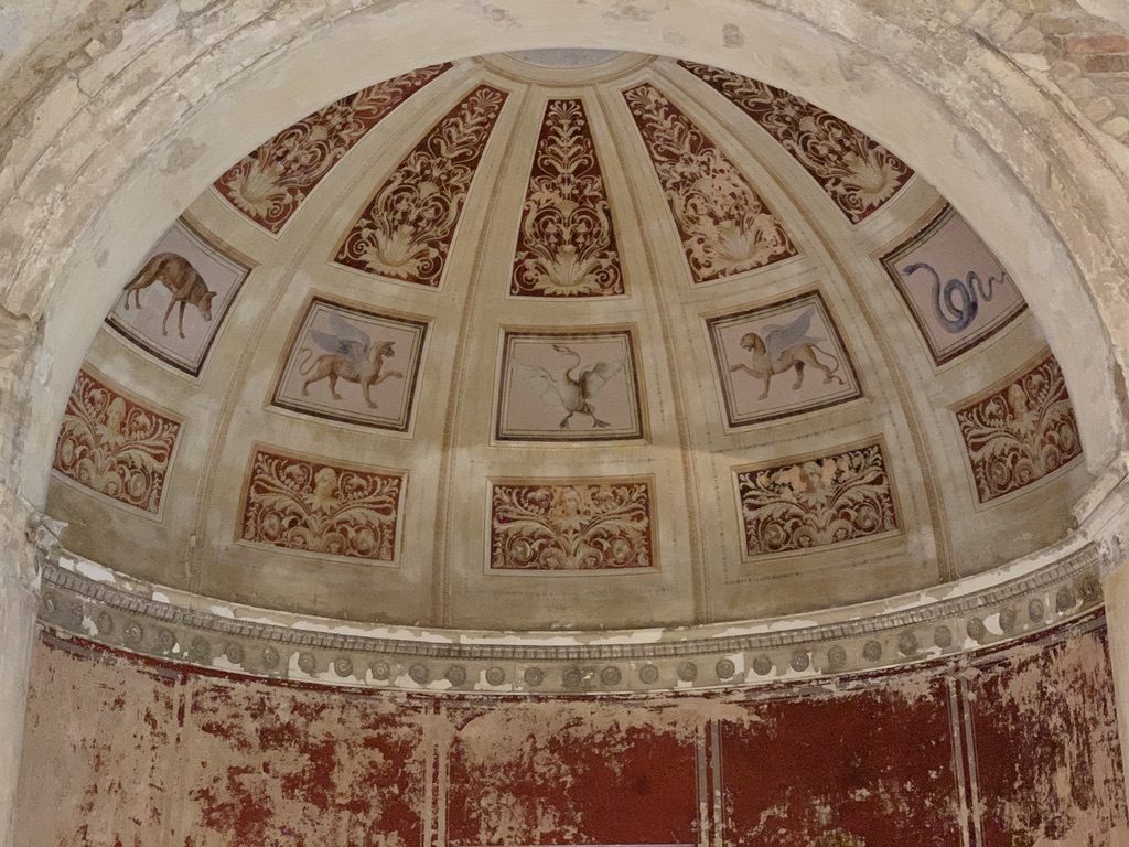 A worn, vaulted ceiling features painted panels with mythical creatures, including a lion with wings and a dragon. The plaster is aged, with faded reds and ornate patterns accentuating the historic architectural design.